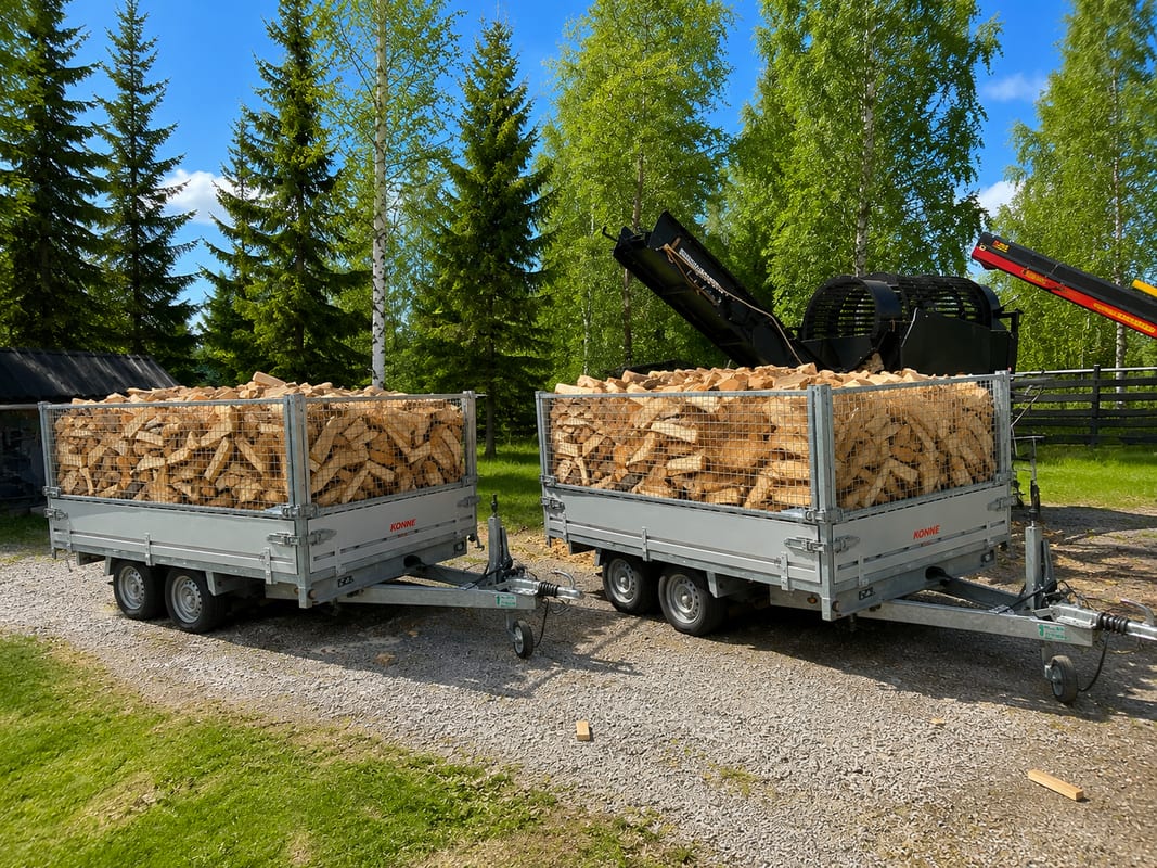 Kaksi verkkolaidallista peräkärryä täynnä kuivaa koivuklapia kesäisellä pihalla